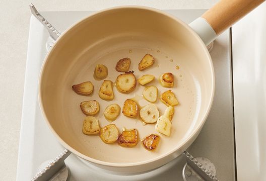 在預熱好的平底鍋裡倒入橄欖油，把蒜片煎至兩面金黃。